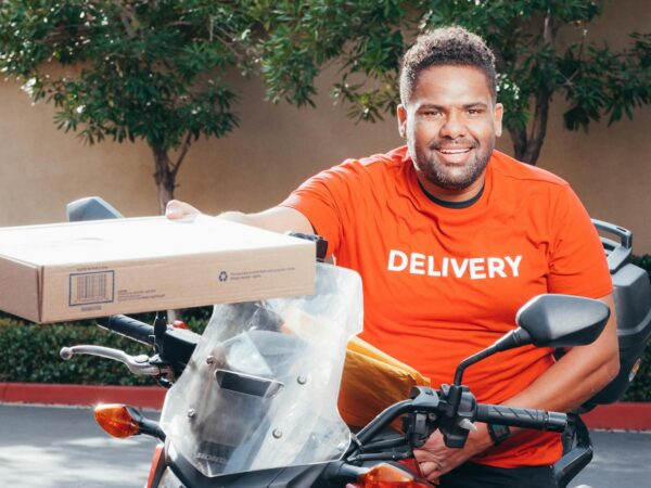 man in red crew neck t shirt sitting on a motorcycle holding a carton box