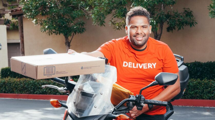 man in red crew neck t shirt sitting on a motorcycle holding a carton box